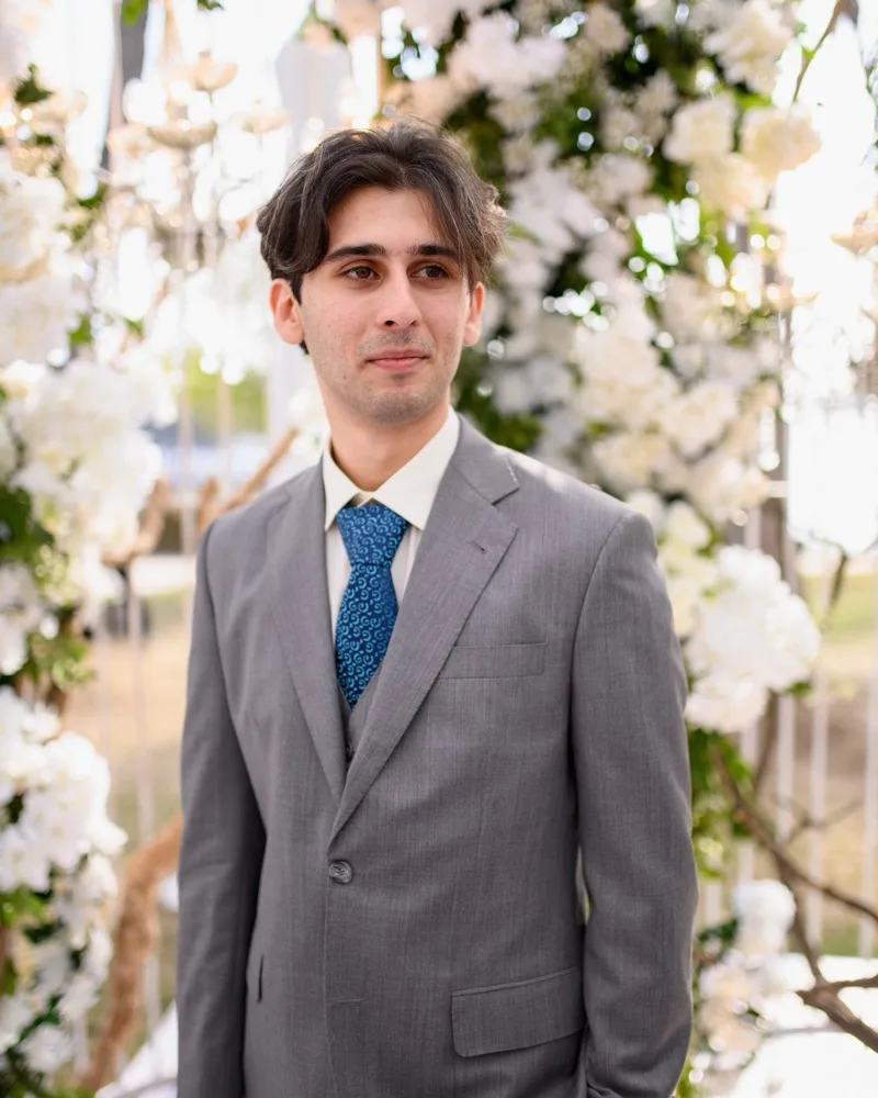 Ali, Kojey's founder, in a grey suit in front of white flowers